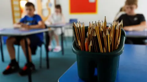 Reuters A pot of pencils in a classroom, with children sitting at desks in the background