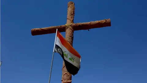 Jewan Abdi Cross with Iraqi flag at entrance to Christian town of Qaraqosh