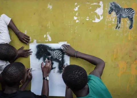 AFP aviour Juma (C), 15, draws zebras by a spray paint on a wall of restaurant during a workshop of Portuguese street artist Ricardo Romero (unseen) as part of his worldwide art project "Project Matilha" which raises awareness of human and animal rights in Kibera slum of Nairobi, on April 25, 2018.