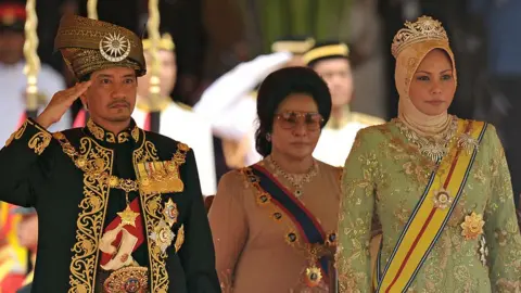 2011 年 12 月 12 日，即将卸任的马来西亚第 13 任国王端姑米占再纳阿比丁（左）和努尔查希拉王后（右）在吉隆坡举行的告别仪式上起立奏国歌。（照片来源：MOHD RASFAN/法新社）来自盖蒂图片社）