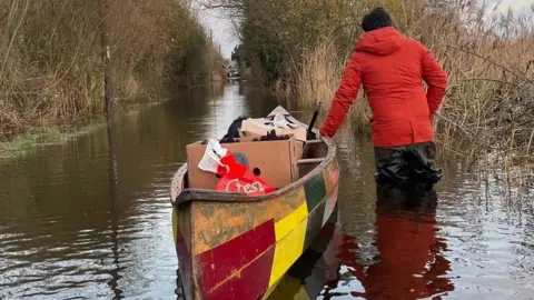 Man with canoe on a flooded road in Surlingham