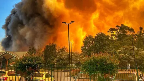 JACKI POCOCK A massive blaze is seen over residential houses and parked cars in Forster on 7 November 2019