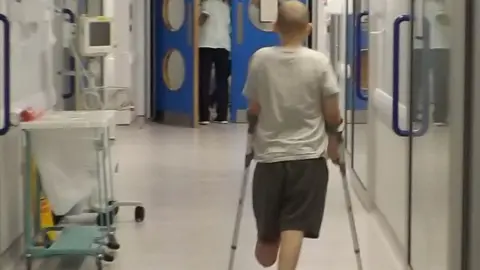 Family handout Alfie walking on crutches in hospital