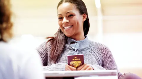 Getty Images Woman holding passport and smiling at airport desk