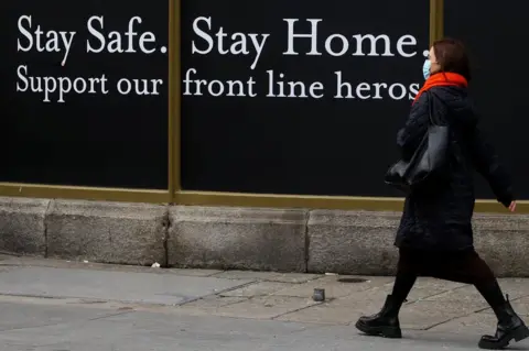 PA Media A woman walks past a shop hoarding which reads: "Stay safe. Stay home. Support our frontline heroes."