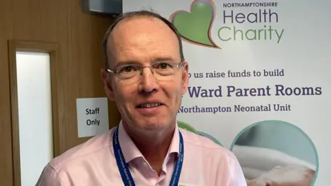 Kate Bradbrook/BBC Dr Nick Barnes, pictured with short dark hair and glasses wearing a lanyard in the hospital