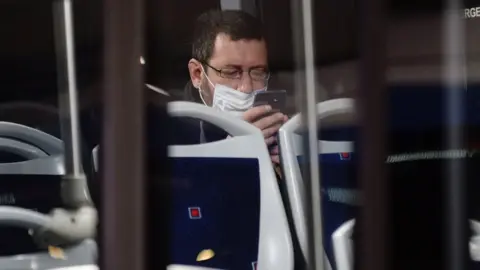 EPA A worker wearing a protective mask looks at his phone on a bus in Valladolid, northern Spain (13 April 2020)