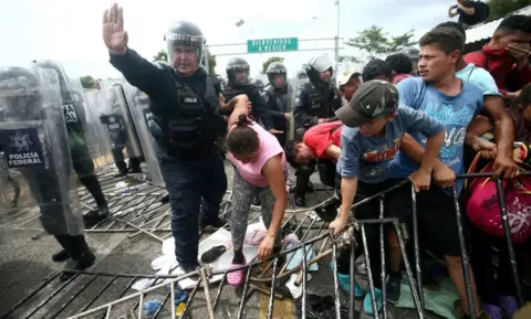 Reuters A police officer holds the arm of a Honduran migrant as she tries to cross a border checkpoint into Mexico