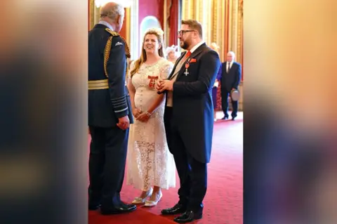 PA Media The King with Sergio and Emma Petrucci wearing their MBEs