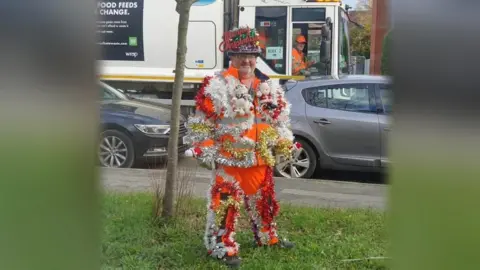 South Cambs DC Bearded man in red festive costume with "Merry Christmas" on his hat, standing in a street