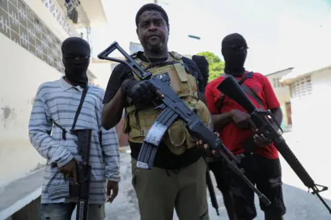 Reuters Former police officer Jimmy "Barbecue" Cherizier, leader of the 'G9' gang alliance, is flanked by gang members after a press conference in Delmas 6, Port-au-Prince, Haiti March 5, 2024.