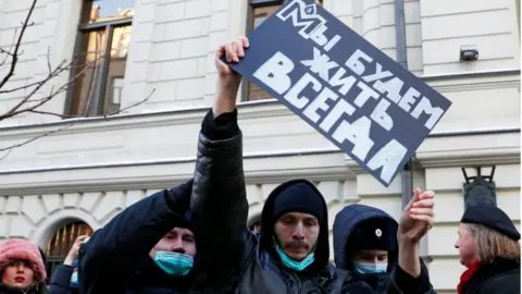 Police officers restrain a supporter of the human rights group International Memorial outside a court building during a hearing of the Russian Supreme Court to consider the closure of International Memorial in Moscow, Russia December 28, 2021. The placard reads: "We will live forever"