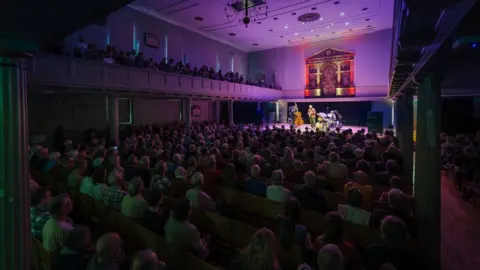 Evan Dawson/St George's A wide shot of St George's in Bristol with audience members seated and the Bill Frisell trio playing on stage