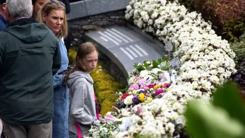 PA Media People gathered at the monument following the service to view the floral tributes left to the victims