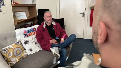 Emma Baugh/BBC Man having a cup of tea in the charity room