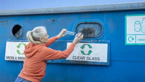 SolStock Woman putting bottle into glass bottle bank