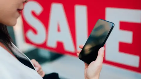 Getty Images Woman with phone next to sale sign