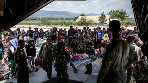 Getty Images Soldiers watch as people board a military plane at Palu airport