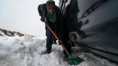 EPA Said, 43, removes snow with a shovel around his vehicle stuck in the snowy and twisty roads, 60km from Azilal city, central Morocco, 05 March 2018 (issued 07 March 2018). Azilal is a city in central Morocco, in the Atlas Mountains,
