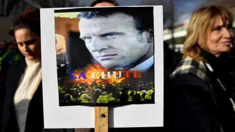 AFP A woman holds a placard bearing a photo of French President Emmanuel Macron with the words "La Chute" (The Fall) during a protest against the pension overhauls, in Marseille, southern France, on 5 December, 2019.