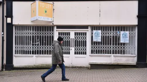 Getty Images Man walking past a boarded up shop