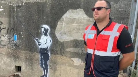 Richard Knights/BBC A security guard protecting a mural in Harwich