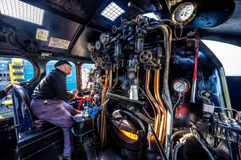 Charlotte Graham / Shutterstock A driver watches the track at the Autumn Steam Gala at the North Yorkshire Moors Railway, UK, on 23 September 2022