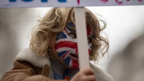 BBC A child with a painted face holds a placard