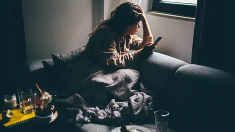 Getty Images Woman sits on a sofa with head in hand