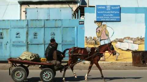 AFP A Palestinian man rides a horse and car past an Unrwa office in Gaza City on 8 January 2018