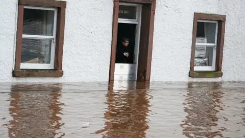 PA Media Karen watches the water from her doorway