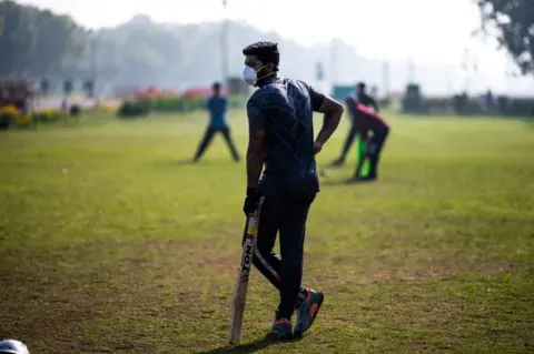 Getty Images A youth (C) wearing a facemask as a preventive measure against the COVID-19 coronavirus plays cricket with his friends at a park in New Delhi on March 18, 2020.