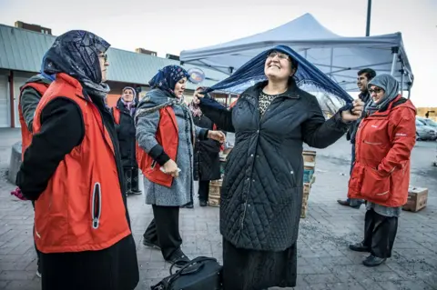 Anette Nantell A group of women gather, with one tying on a headscarf.