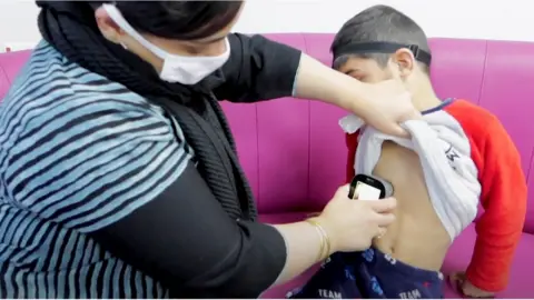 BTHFT A mother holds the device to her son's chest so that medical staff can hear his breathing