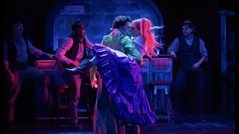 Ali Wright Brightly lit theatre stage. Two people dancing in colourful cowboy themed outfits