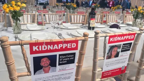 Rows of laid tables with empty seats and posters of missing people, at the event.