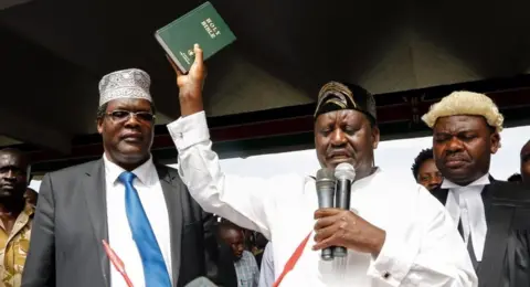 EPA Raila Odinga raises a bible as he "takes an oath" during an unofficial "swearing-in" ceremony in Nairobi on 30 January 2018.