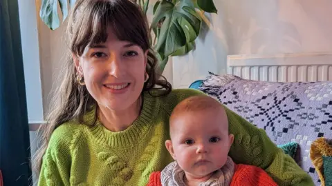 Hanna Jarman with infant on her knee sitting in their lounge