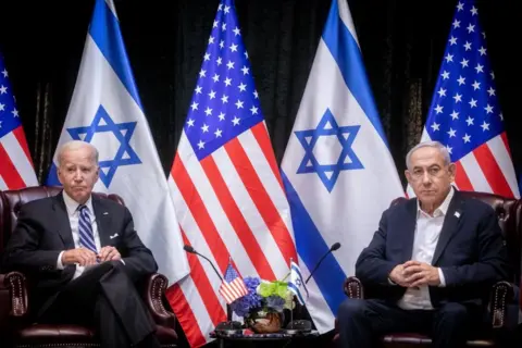 Getty Images US President Joe Biden sits with Israeli Prime Minister Benjamin Netanyahu at the start of the Israeli war cabinet meeting in Tel Aviv on 18 October against a backdrop of Israeli and American flags