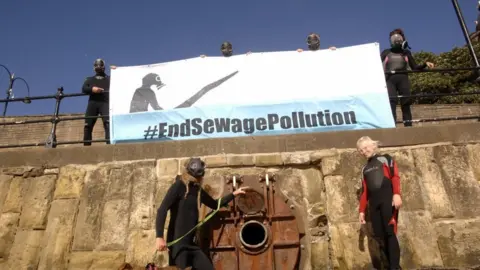 Steve Crawford Surfers holding a banner calling for the end of sewage dumping in Scarborough, North Yorkshire