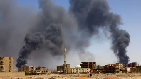 Reuters A man walks while smoke rises above buildings after aerial bombardment, during clashes between the paramilitary Rapid Support Forces and the army in Khartoum North, Sudan, May 1, 2023.