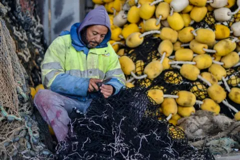 Getty Images A fisherman preparing a fishing net on his boat at the port of Zarzis in the southern coast of Tunisia - Saturday 7 January 2023