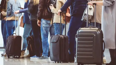 Getty Images Passengers queuing with their luggage in an airport.