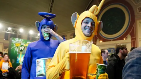 PA Media A general view of fans before the final of the Paddy Power World Darts Championship at Alexandra Palace, London, with two men carrying beer and dressed up like the Teletubbies