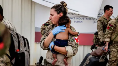 UK MOD An Army paramedic holds a baby during evacuation of British nationals in Sudan