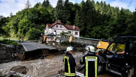 EPA Firefighters next to a damaged road after flooding in Schuld, Germany