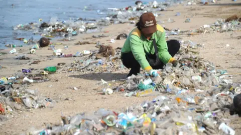 AFP/Getty Images Person collecting rubbish at Kuta beach