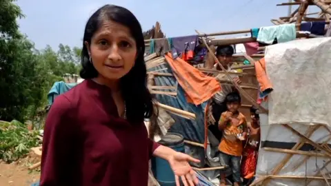 Rajini Vaidyanathan in front of a partially destroyed hut