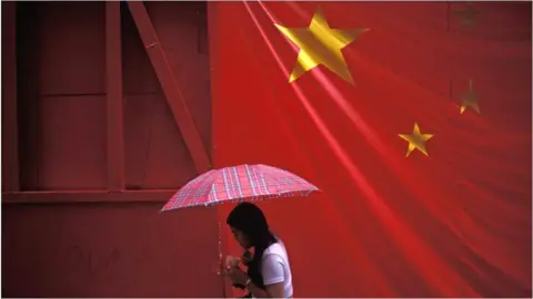 Getty Images A large banner Chinese flag hangs over a pedestrian on the eve of the handover of sovereignty from Britain to China, on 30 June 1997, in Hong Kong, China.