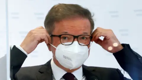 Reuters Austrian Health Minister Rudolf Anschober adjusts his face mask during a news conference in Vienna, 13 April